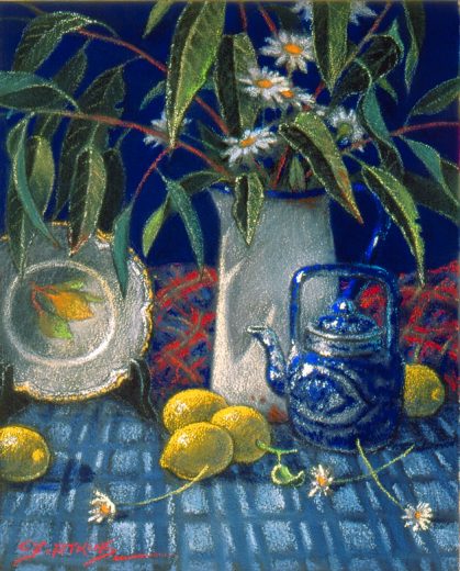 Gum leaves in an enamelware jug accompany yellow lemons on a blue patterned cloth.