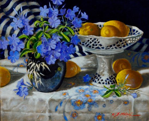 Lemons in a cut out bowl stand beside a vase of plumbago flowers.