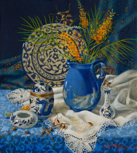 Grevillea flowers in a blue jug and a ceramic with a dragon motif stand on a table.