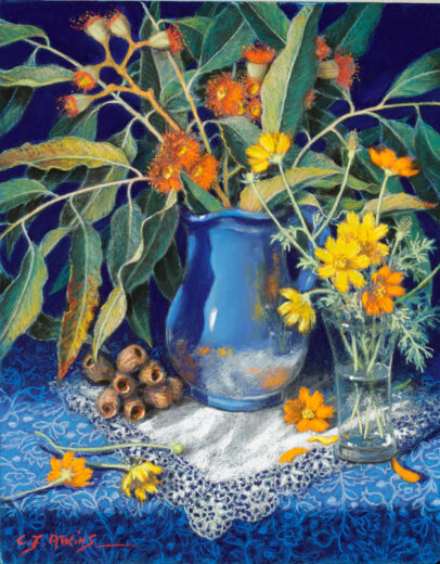 Orange gum blossoms are in a blue vase accompanied by cosmos in a glass vase.