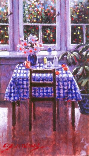 A table stands in front of a window. A vase of flowers and other items are on the table.