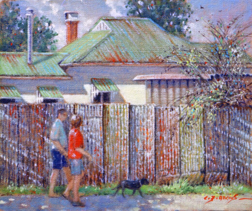 Another couple walk with their dog on the footpath in front of an old metal fence.