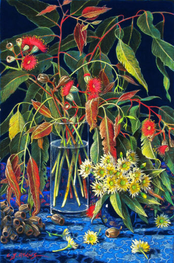 Eucalypt leaves and flowers spill out of a tall glass vase.