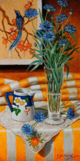 Cornflowers in a glass vase are accompanied by a jug with a MakMerry design.