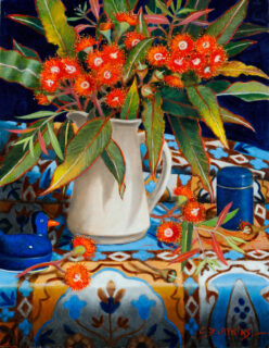 A pale jug contains bright red eucalypt flowers.