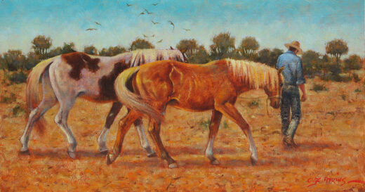 A man leads two horses in a dry and dusty paddock.
