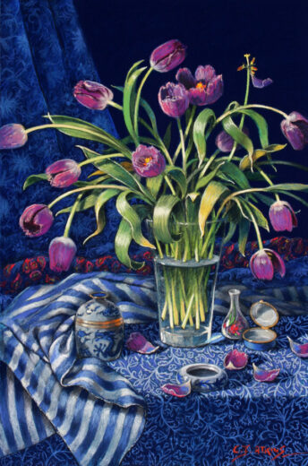 Tulips in a glass vase resting on or near several patterned cloths.