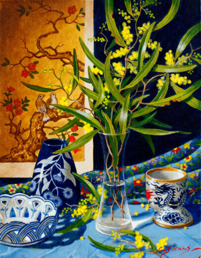 Australian ball wattle flowers are in a glass vase accompanied by items with an Asian theme.