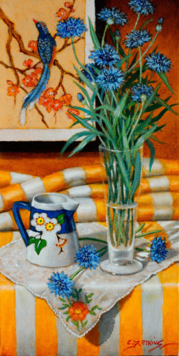 Corn flowers in a vase are in front of an Asian-themed wall hanging.