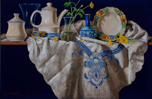 An embroidered cloth is draped over a shelf and a ceramic coffee pot rests on it along with several other items.