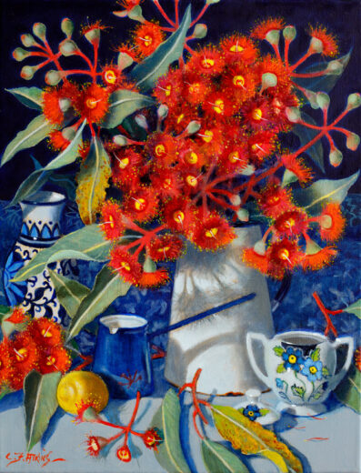 An enamel coffee pot of bright red gum blossoms is accompanied by a single lemon and other objects. 