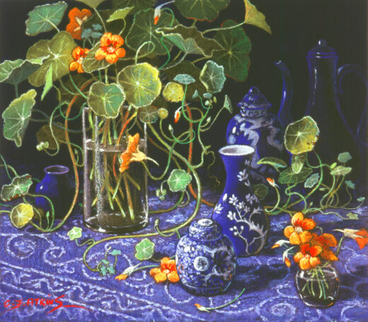 Nasturtiums in a glass vase and several other objects rest on a richly decorated tablecloth.