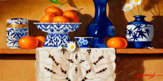Blue and White ceramics, including a bowl holding mandarins stand on a shelf. A lace doily hangs down from the shelf.