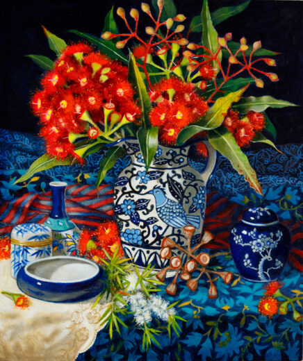 Red flowers and green leaves are displayed in a jug with a bird motif.