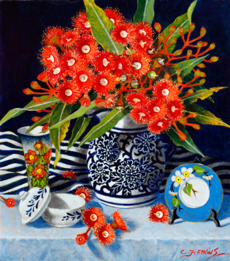 Bright red flowers and deep green leaves are in a decorated bowl.